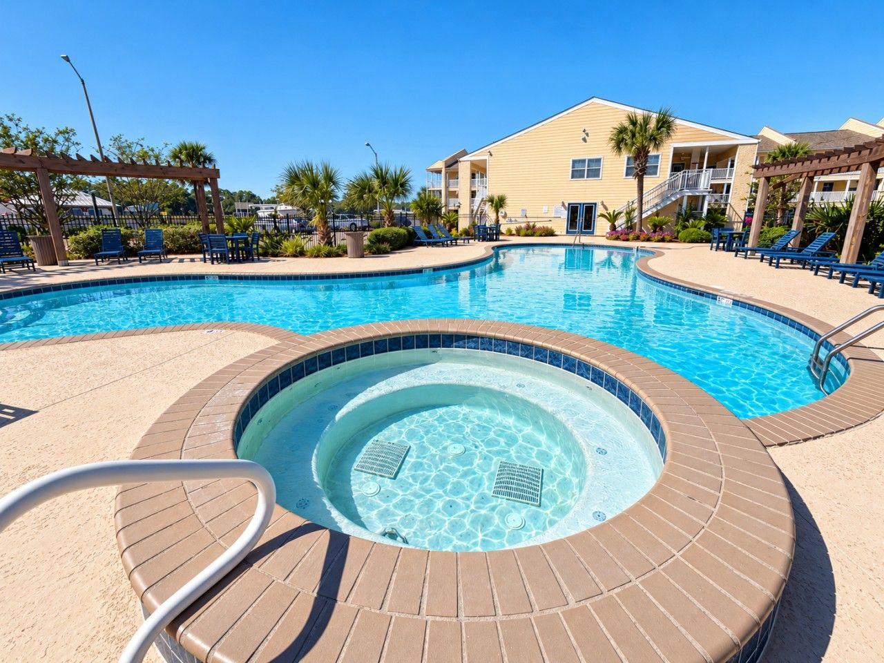 A swimming pool with a hot tub, lounge chairs, and a building in the background.