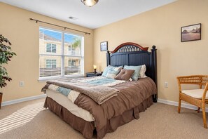 A bedroom with a bed, a window, a nightstand, a chair, and a wall-mounted picture. - Slip Away at Harbor Landing (Ocean Springs)