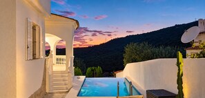 A pool area with a view of a hill and sunset.