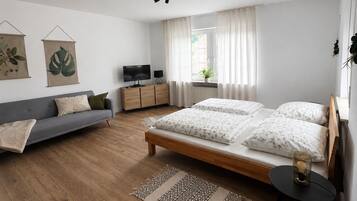 Ein modernes Schlafzimmer mit Bett, Sofa, Fernseher und einem Fenster mit Vorhängen.