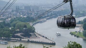 Eine Seilbahn über einem Fluss, im Hintergrund eine Stadtansicht.