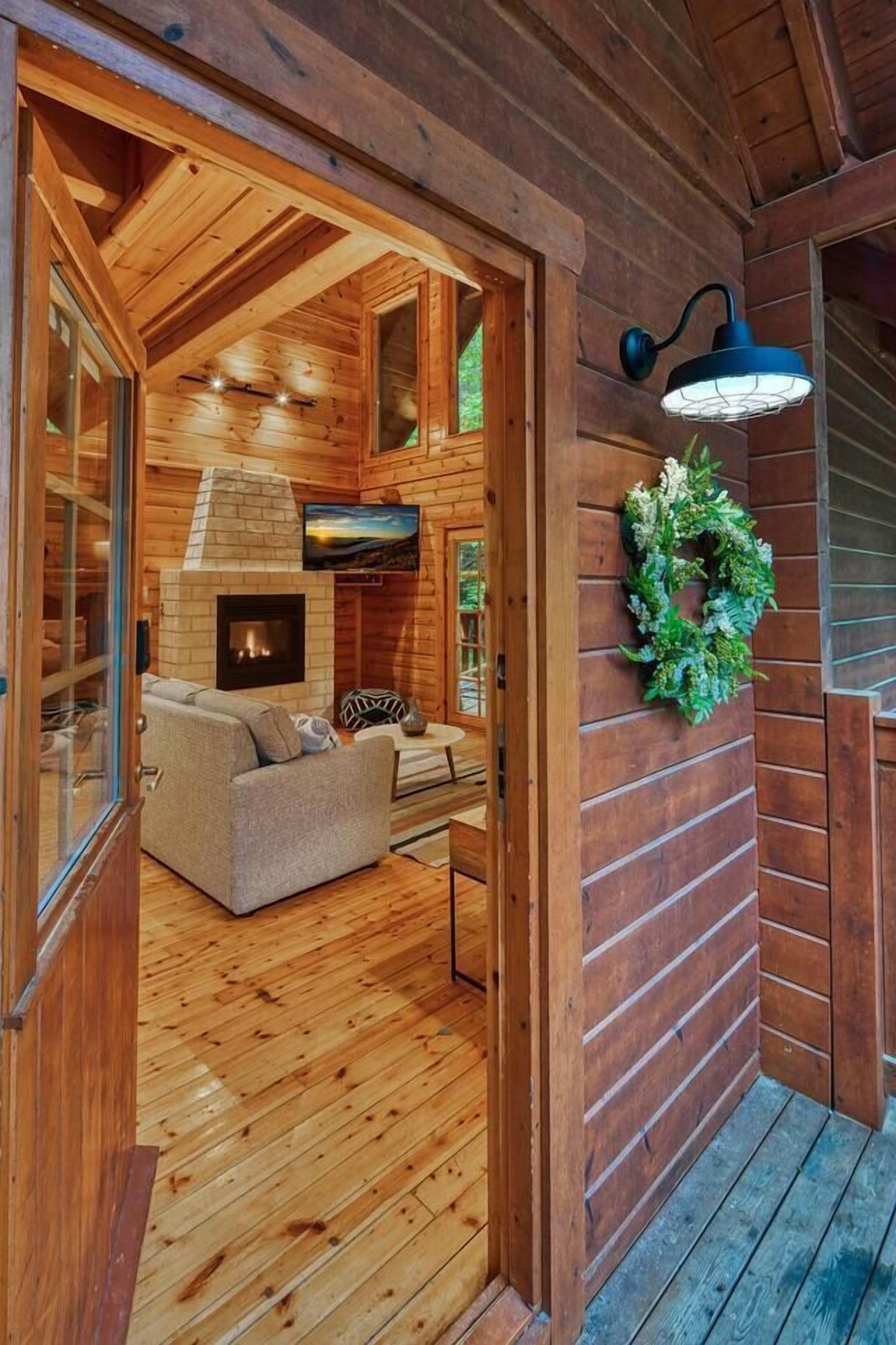 A wooden cabin interior with a fireplace, a sofa, and a wall-mounted light fixture.
