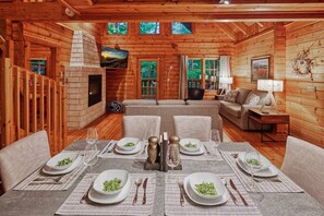 A cozy log cabin interior with a dining area set for a meal, a fireplace, and a television. - Romantic Cabin | Sauna & Hot Tub near Dollywood (Sevierville)