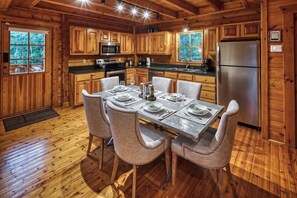 A wooden cabin interior with a dining table set for four, kitchen appliances, and a large window. - Romantic Cabin | Sauna & Hot Tub near Dollywood (Sevierville)