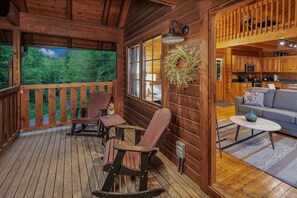 A wooden cabin with a deck, rocking chairs, a sofa, and a kitchen area. - Romantic Cabin | Sauna & Hot Tub near Dollywood (Sevierville)