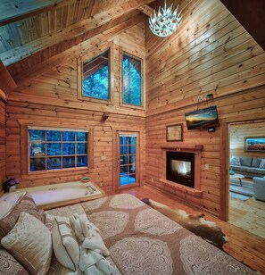 A log cabin interior with a fireplace, large windows, and a television. - Romantic Cabin | Sauna & Hot Tub near Dollywood (Sevierville)