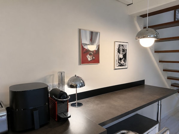 Uma cozinha moderna com balcão, máquina de café e duas obras de arte emolduradas na parede.