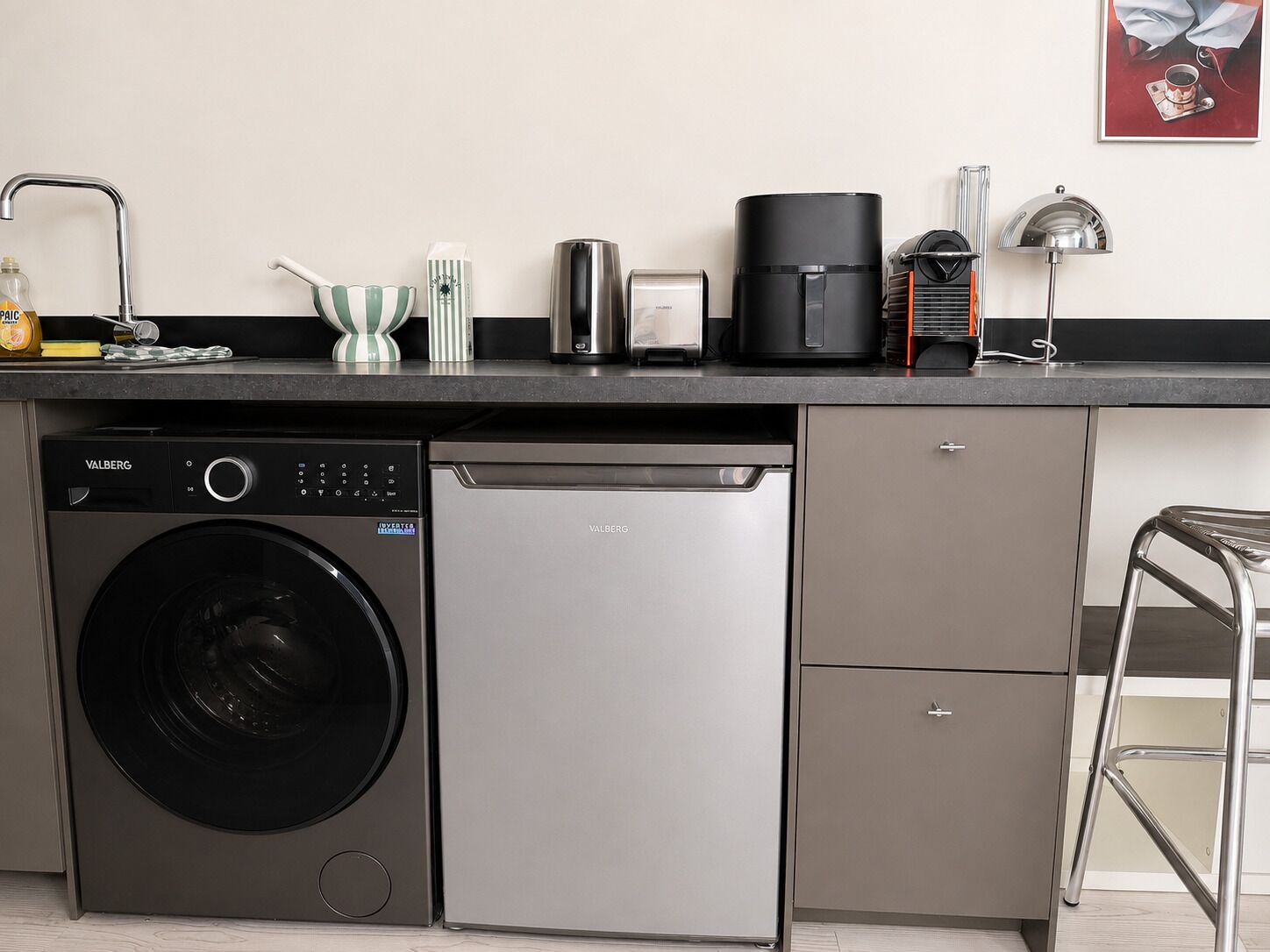 Une cuisine compacte équipée d’un lave-linge, d’un lave-vaisselle et d’une machine à café posée sur le plan de travail.