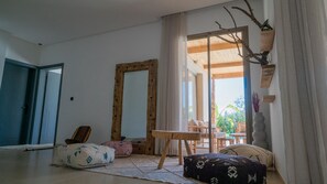 Ein Zimmer mit einem großen Spiegel, einem Holztisch, einer Couch und Blick ins Freie.