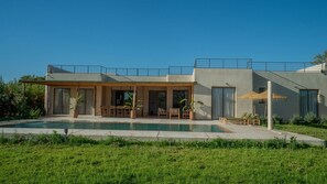 Ein modernes Haus mit Swimmingpool, Sitzgelegenheiten im Freien und einer überdachten Terrasse.