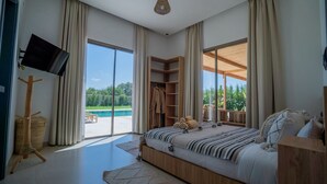 Un dormitori amb un llit gran, televisió, armari de fusta i vista a una piscina.