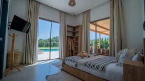Ein Schlafzimmer mit einem großen Bett, einem Fernseher, einem Holzschrank und Blick auf einen Swimmingpool.