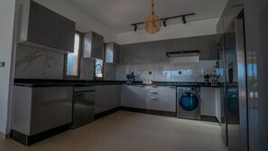 Une cuisine moderne dotée d’appareils électroménagers en acier inoxydable, d’un lave-linge encastré et d’un luminaire suspendu.