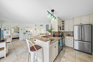 Uma cozinha moderna com ilha central, eletrodomésticos de aço inoxidável e área de jantar com cadeiras brancas.