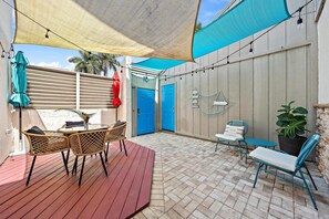 A patio with a wooden deck, wicker chairs, a table, a potted plant, and a blue door. - SummerSalt - 5 Min Walk To Beach! (Jupiter)