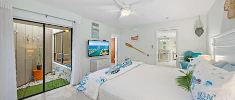 A bedroom with a bed, a television, a ceiling fan, and a view of the outside.