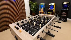Ein Tischkicker in einem Raum mit leuchtendem Neon-Controller-Schild, Spielautomaten und einer Topfpflanze.