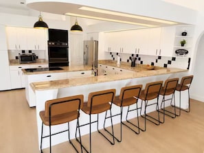 A modern kitchen with a central island, bar stools, and built-in appliances. - Heated Pool, Arcade, Home Theater, Outdoor Dining (Cape Coral)