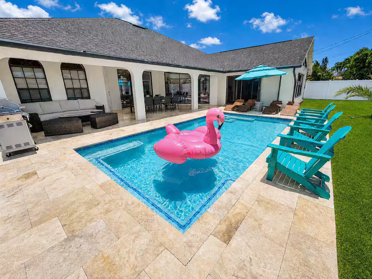 Ein Swimmingpool mit einem rosa aufblasbaren Flamingo, umgeben von Liegestühlen und einer überdachten Terrasse.