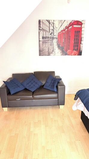 Ein Zimmer mit einer schwarzen Ledersofa, Holzboden und einem roten Gemälde einer Telefonzelle an der Wand.