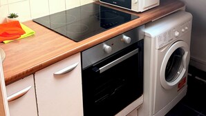 A compact kitchen with a microwave, oven, and washing machine, a small window, and white tiled walls. - Apartment Sleeps 6 With Wifi in Willesden Green (London)