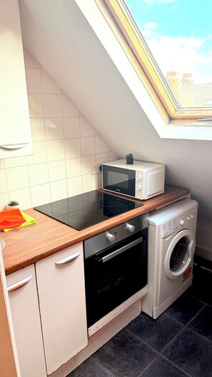 Eine kompakte Küche mit Mikrowelle, Backofen und Waschmaschine, einem kleinen Fenster und weiß gefliesten Wänden.