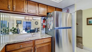 A kitchen with wooden cabinets, a stainless steel refrigerator, a marble countertop, and a ceiling light fixture. - 2-bedroom, 2 floor condo in beautiful Fort Myers Beach! (Fort Myers Beach)