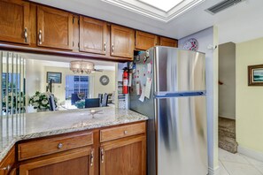 A kitchen with wooden cabinets, a stainless steel refrigerator, a marble countertop, and a ceiling light fixture. - 2-bedroom, 2 floor condo in beautiful Fort Myers Beach! (Fort Myers Beach)