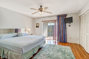 A bedroom with two beds, a ceiling fan, a TV mounted on the wall, and a sliding glass door leading to a balcony. - 2-bedroom, 2 floor condo in beautiful Fort Myers Beach! (Fort Myers Beach)