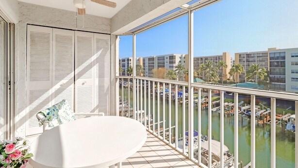 A balcony with a ceiling fan, a white table, and a view of a marina with boats and buildings. - 2-bedroom, 2 floor condo in beautiful Fort Myers Beach! (Fort Myers Beach)