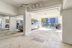 Un parking avec des piliers en béton, une voiture garée sous un abri, et un bâtiment avec une marina en arrière-plan.