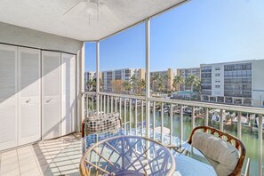 Un balcon avec une table en verre, des chaises en osier et une vue sur une marina avec des bateaux et des bâtiments.