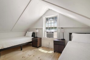 Une chambre avec deux lits simples, une fenêtre avec des stores et un ventilateur de plafond.