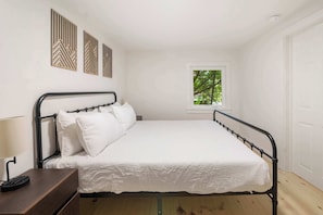 Una cama individual con estructura metálica, ropa de cama blanca y una mesita de noche con lámpara. Encima de la cama, tres paneles decorativos fijados a la pared.