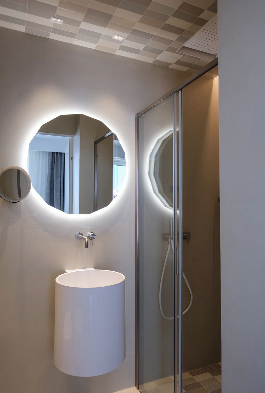 A modern bathroom with a round mirror, a sink, and a glass shower enclosure.