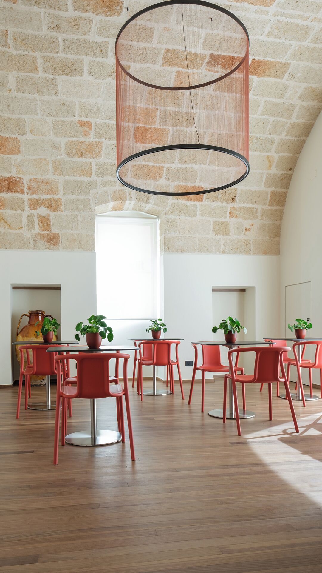 Una habitación con pared de piedra, lámpara colgante, sillas rojas y plantas en macetas.