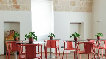 Una habitación con pared de piedra, lámpara colgante, sillas rojas y plantas en macetas.