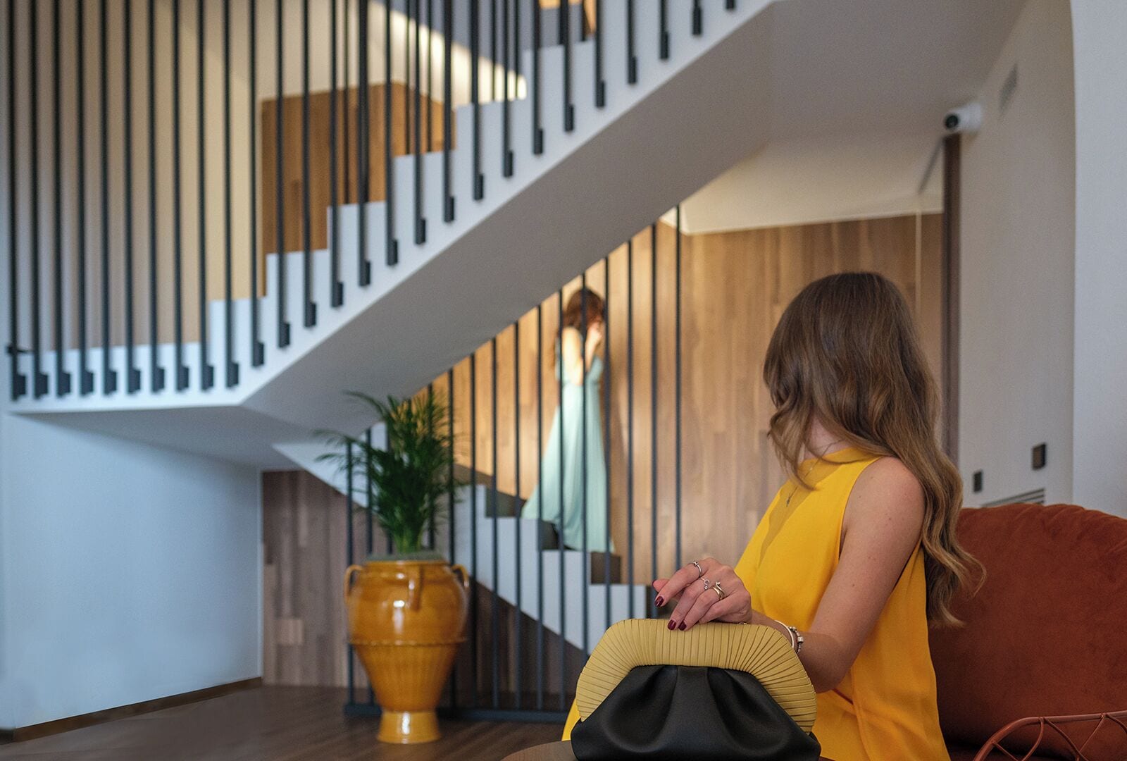 A woman sitting on a sofa in a modern interior with a staircase and a large vase.