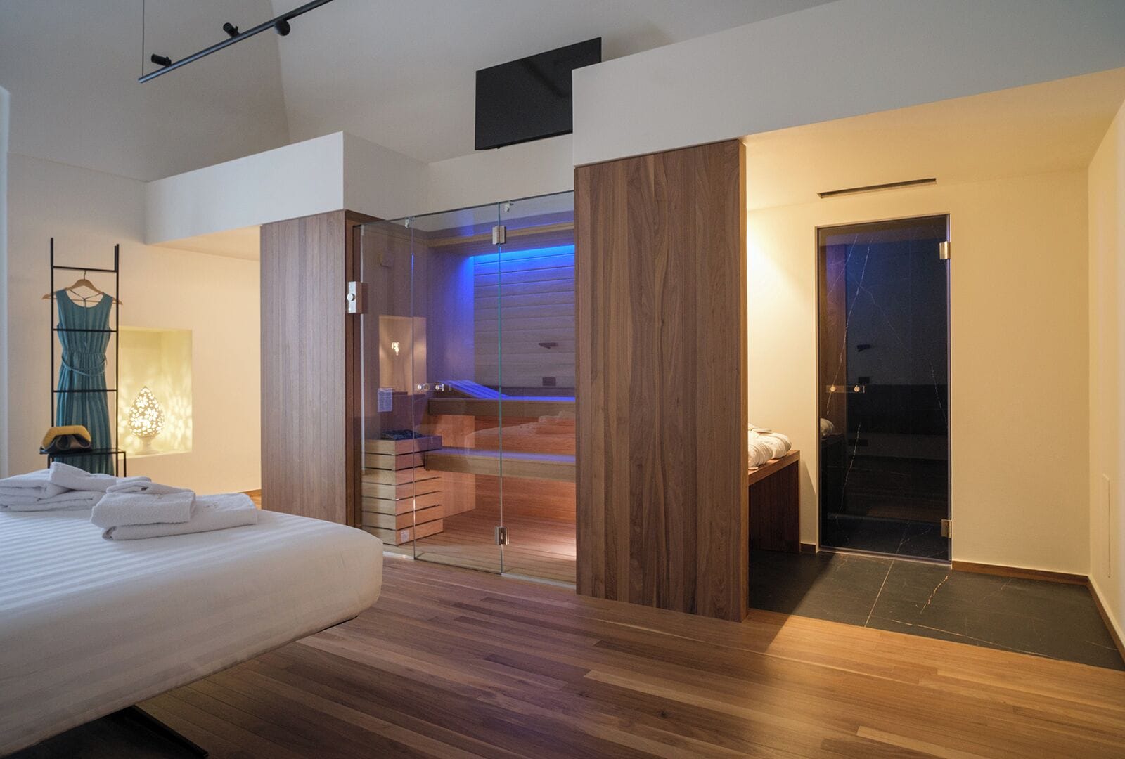 A modern bedroom with a large bed, a glass-enclosed walk-in closet, and a visible bathroom with a bathtub.
