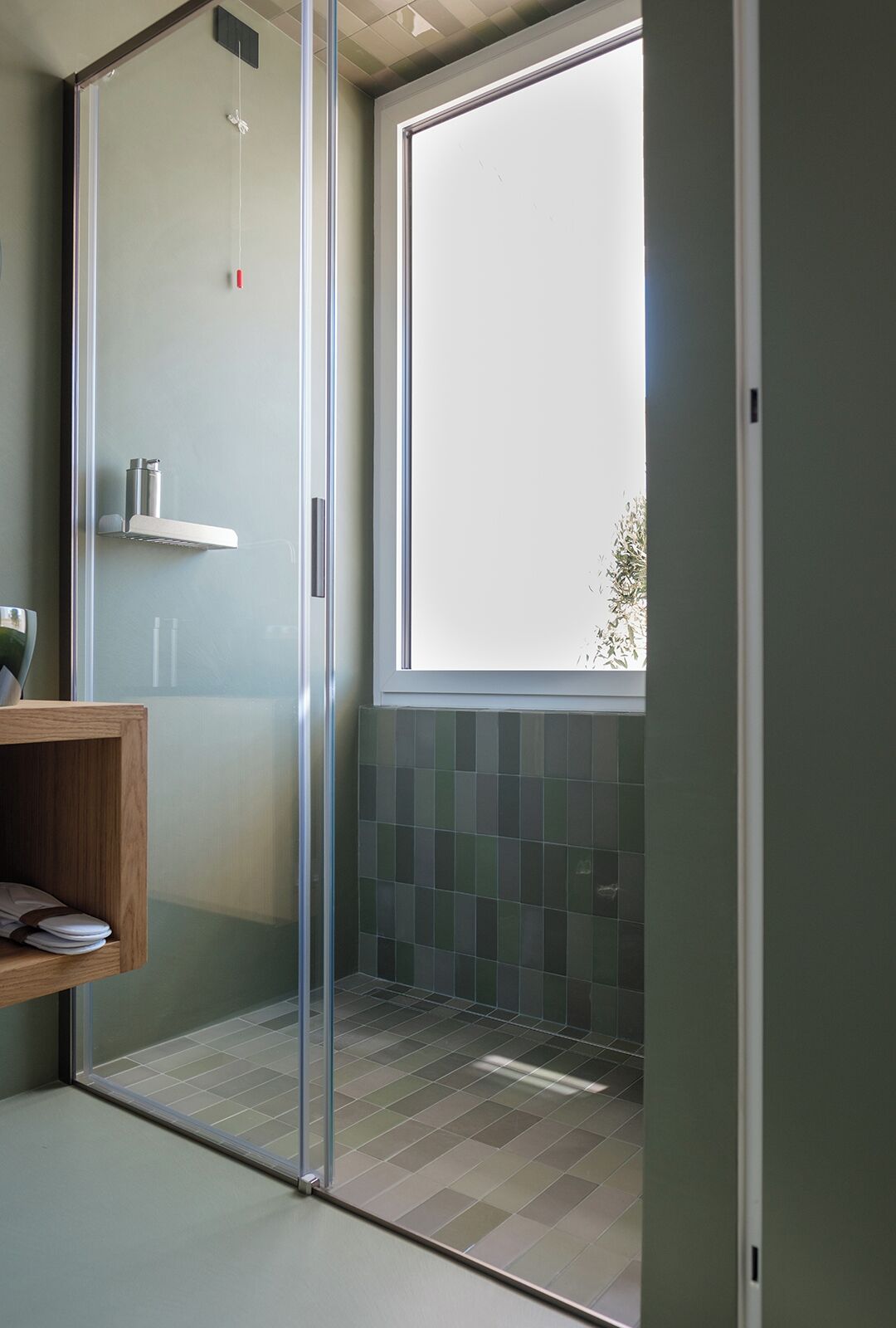 Une salle de bain moderne avec une porte de douche en verre, une fenêtre, une étagère en bois et un carrelage au sol.
