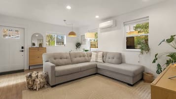A modern living room with a grey sectional sofa, wooden cabinet, and a large window with a view of greenery.