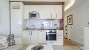 Eine kleine Küche mit weißen Schränken, einer Mikrowelle, einem Backofen und einem Spülbecken.