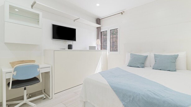 Ein Schlafzimmer mit einem Bett, einem Schreibtisch mit Stuhl, einem Fernseher und einem Fenster.
