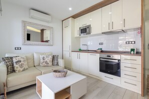 A modern kitchen with white cabinetry, a microwave, an oven, and a dining area with a white table and a woven basket. - Home2Book Sea View Pool & Terrace Las Burras Beach (Maspalomas)