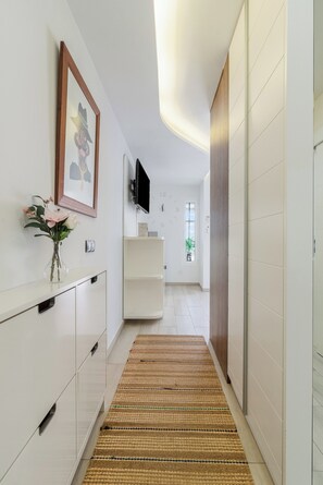 A hallway with a flat-screen TV mounted on the wall, a framed picture above a white cabinet, and a woven rug on the floor. - Home2Book Sea View Pool & Terrace Las Burras Beach (Maspalomas)