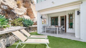 Ein modernes Haus mit einer Terrasse, ausgestattet mit zwei Liegestühlen und einem Esstisch mit Stühlen.
