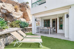 Ein modernes Haus mit einer Terrasse, ausgestattet mit zwei Liegestühlen und einem Esstisch mit Stühlen.