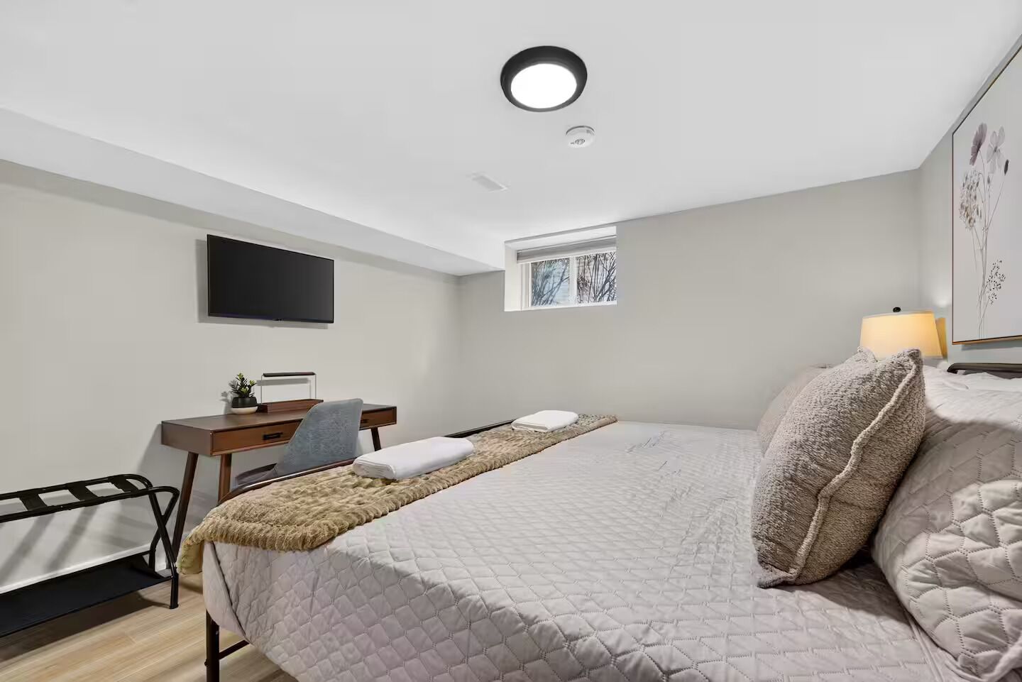 Une chambre à coucher avec un lit, un bureau, une chaise, une télévision, une fenêtre et une lampe.