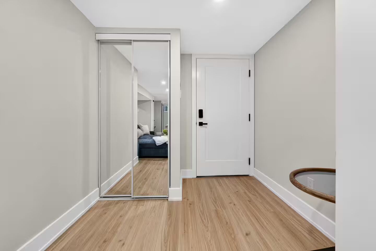 Een hal met een schuifdeur naar een slaapkamer, een witte deur en een houten vloer.