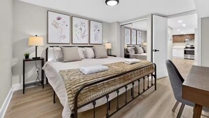 Een moderne slaapkamer met een bed, nachtlampjes, een nachtkastje met een plant en een grote spiegel.